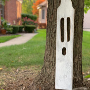 Large handmade white wooden ghost leaning against a tree trunk