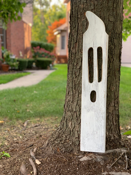 Large handmade white wooden ghost leaning against a tree trunk