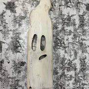 Handmade white wooden ghost with carved face on black-and-white toile