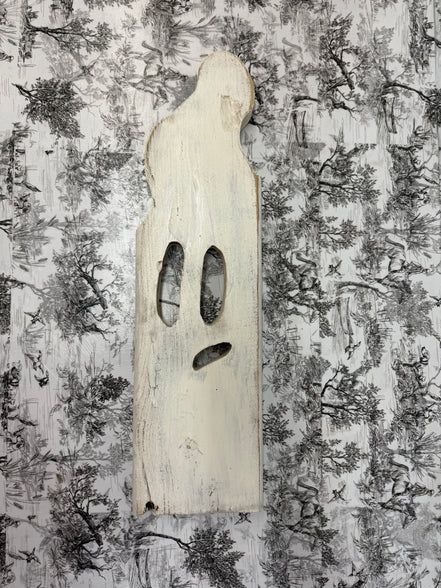 Handmade white wooden ghost with carved face on black-and-white toile